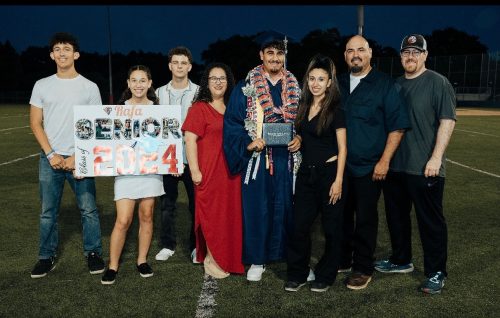 Rios family posing together on a football field to celebrate a graduate holding a diploma, with a "Senior 2024" sign.