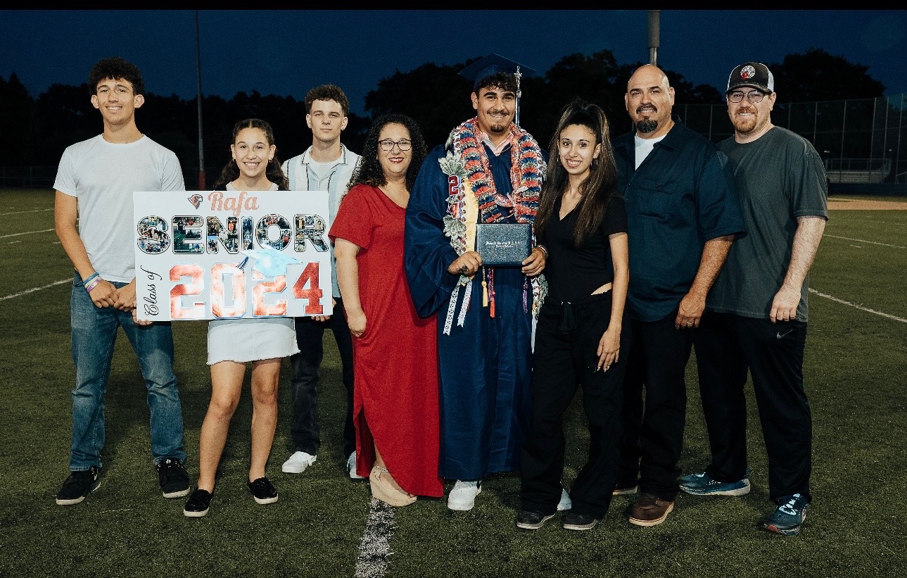 Rios family posing together on a football field to celebrate a graduate holding a diploma, with a "Senior 2024" sign.