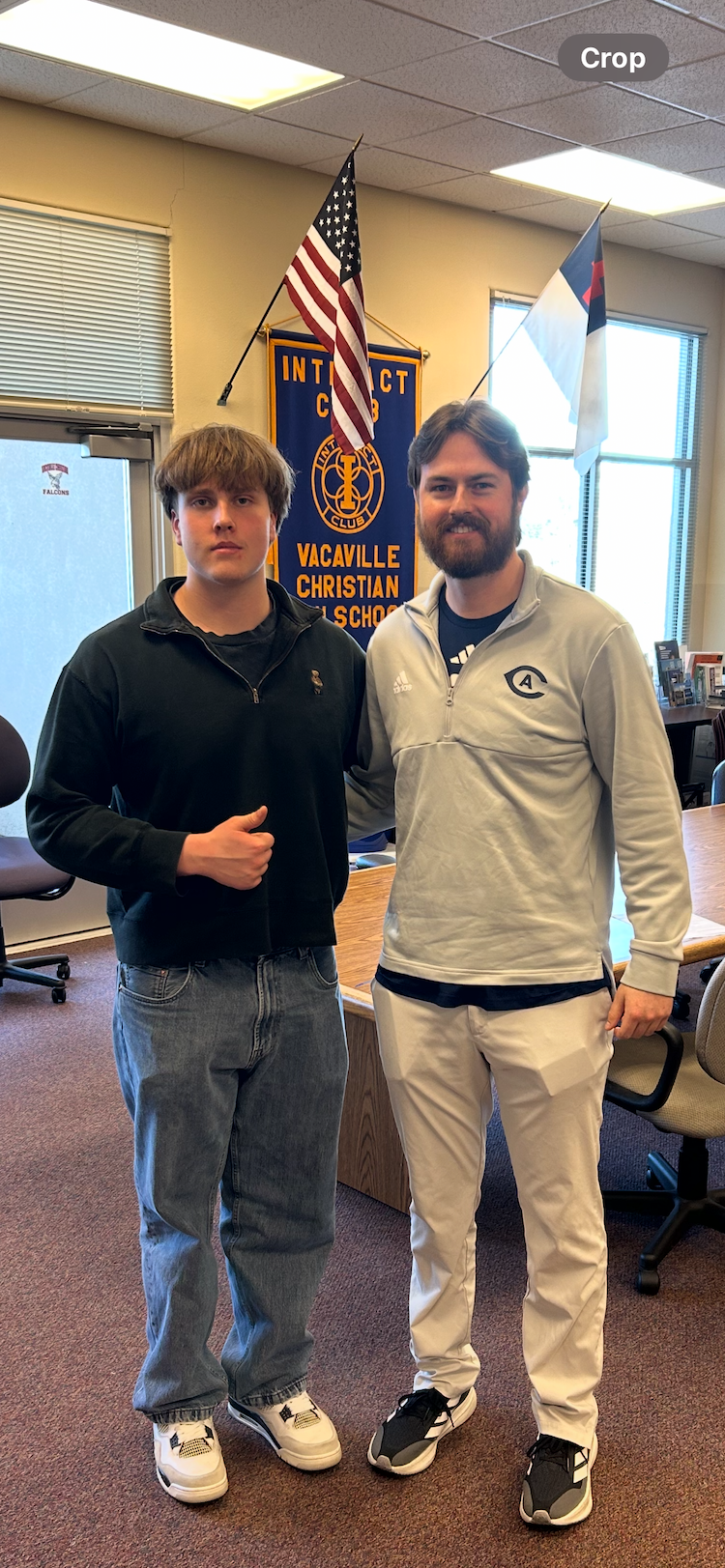 Two males stand together inside a school office with an American flag and a Vacaville Christian School banner behind them.