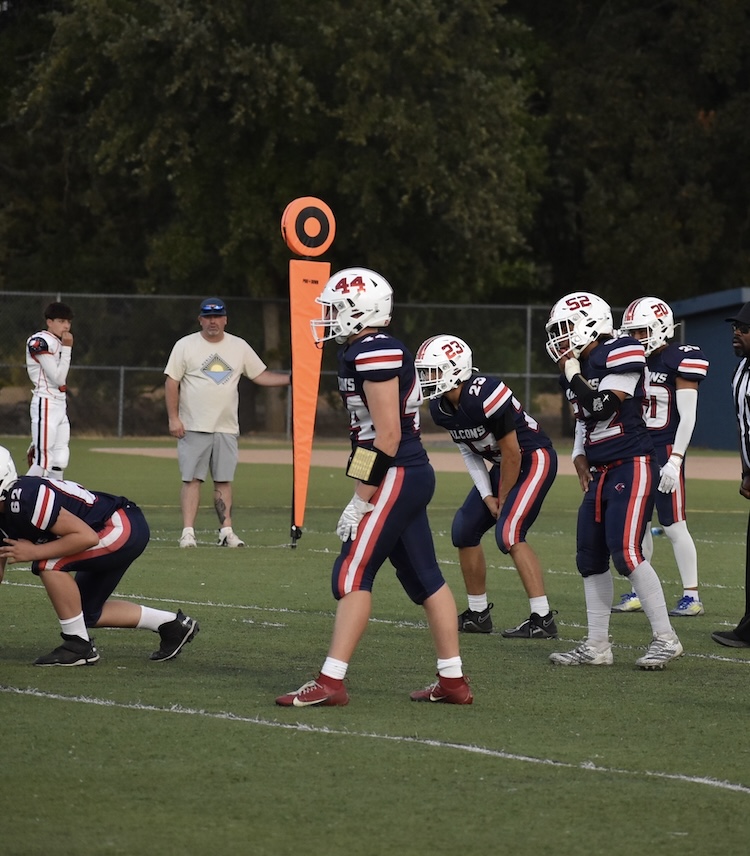 High school football players in navy and red uniforms line up before a play on the field.