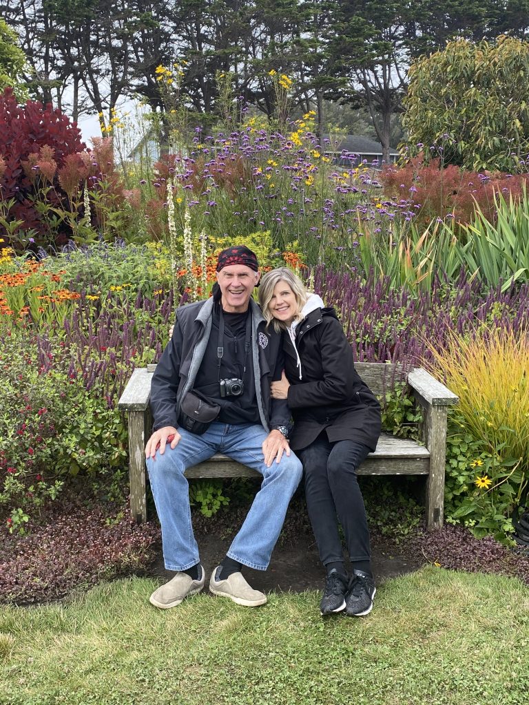 Couple sitting together on a wooden bench surrounded by a colorful flower garden
