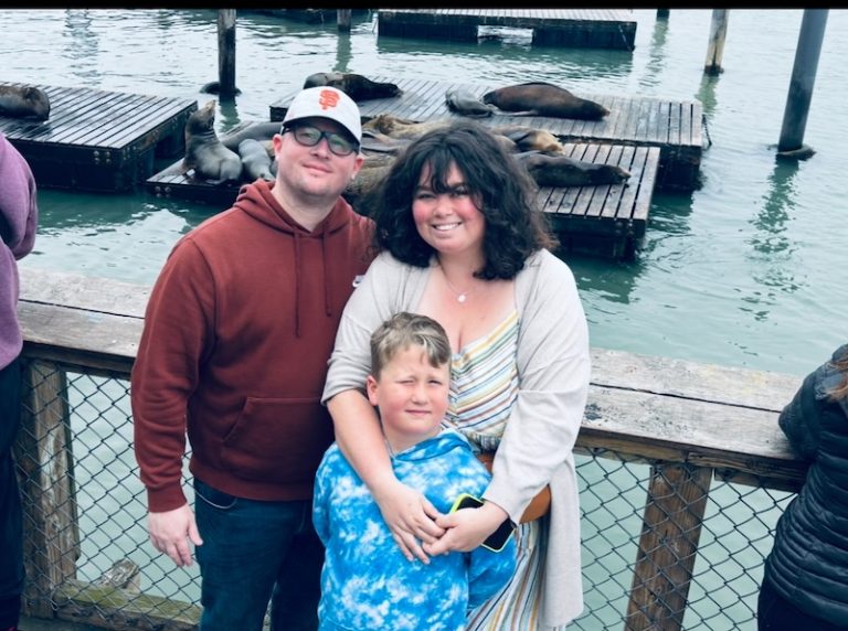 Family standing together on a waterfront pier with sea lions resting on docks behind them