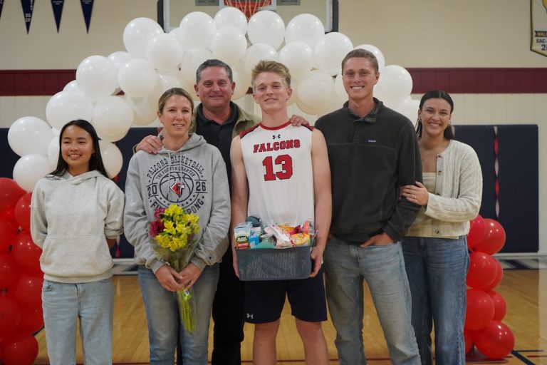 High school basketball player in a Falcons jersey standing with family members under a balloon arch, holding flowers and a gift basket.