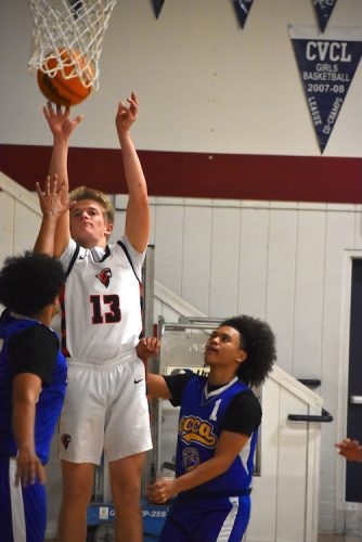 Basketball player wearing number 13 jumping for a layup while two defenders contest the shot in a gym.