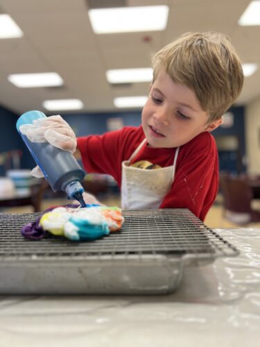 VCS elementary student pouring blue dye onto fabric during an art activity